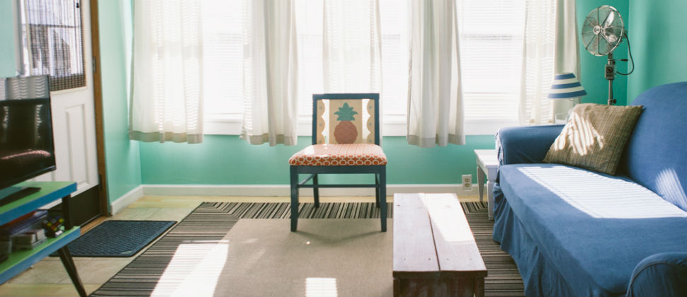 cottage one living room with blue couch, orange and white chair with pineapple design on back and a tv