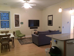 livingroom with grey couch, green side chair wall mounted TV and white ceiling fan.