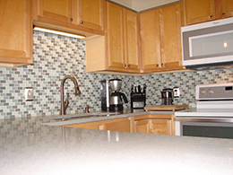 Kitchen with tan cabinets, grey counter tops, blue/grey patterened backsplash.