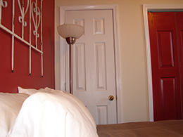 side view of a queen bed with white pillows and stainless steel floor lamp and white door.