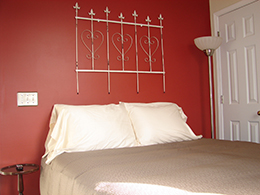 Queen bed with tan duvet and white pillows against a rich red wall.