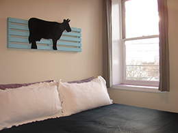 King bed with white pillows and wall art of a blue fence and black cow.