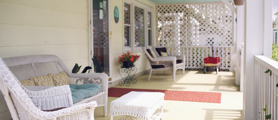 front porch of the inn with white whicker furniture, yellow siding, light blue ceiling and red wagon in the background