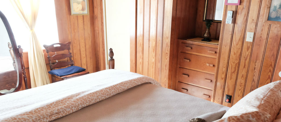 Pineapple room on the second floor with a queen bed, tan blanket and wood antique chair with blue cushion