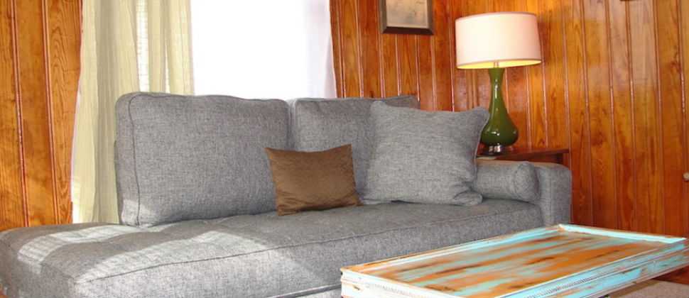 Seating area with grey chaise lounge sofa with natural light touching one end, green vintage lamp on end table.