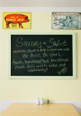 breakfast table with white salt and peper shakers, green candle and wall chalkboard that reads savory or sweet motto