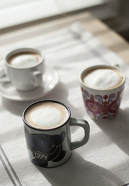 three cups of espresso with foam in a red patterned cup, a white teacup and a cup with the design 1971