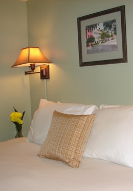 queen bed with a tan throw pillow in front of four white pillows.  Yellow flowers on the nightstand