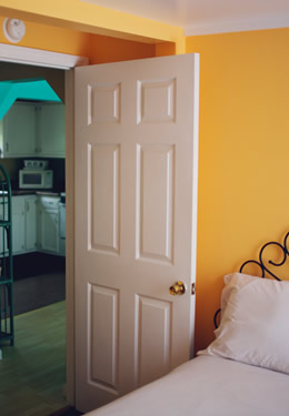 full bed with orange colored walls, a white open door showing the kitchen in the background