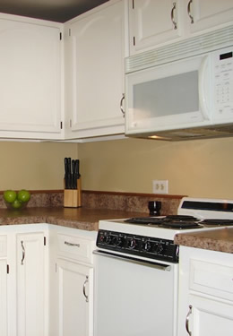 cottage one kitchen with dark countertops, white cabinets and a clear bowl displaying three green apples