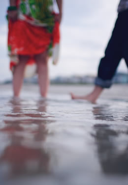 two people splashing feet - man with pants rolled up and woman holding green and red dress up from the water