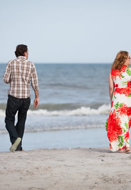 woman with flowing tropical dress and man with pant cuffs rolled seen from the back walking toward the blue ocean