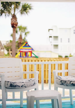 two white patio chairs on the aqua painted porch of cottage 2 with a palm trees in the background