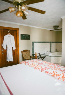 queen size bed with red and white duvet, white luxury robes hanging behind the door and whilrpool tub in background