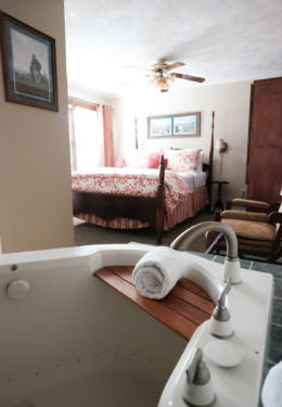 Whirpool tub with queen bed in background covered with red and white duvet and brown four corner bed posts.