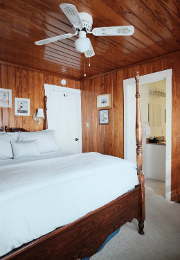 Queen bed with light blue duvet on a brown wood four post bed frame and a peek into the bathroom.