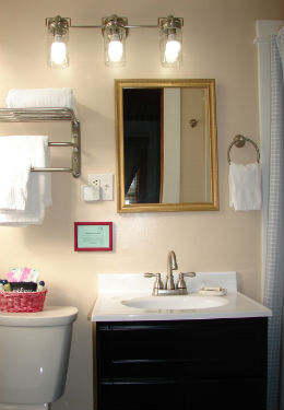 bathroom with black vanity, white sink and brush nickel faucet. White towels draped over shelf rack and hand towel ring.