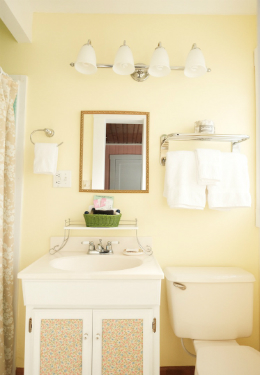 yellow painted bathroom with white luxury towels hanging on a rack and a green basket on a white vanity