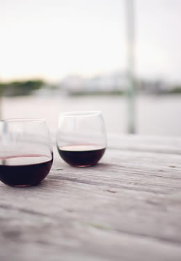 red wine in two stemless glasses set on wooden pier with the sun setting on the canal in the background