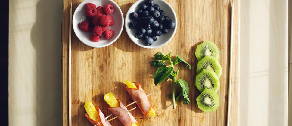 red raspberries, blueberries, pineapple wrapped in Canadian bacon and green parsley on wooden cutting board